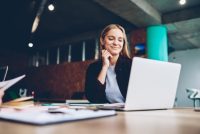 Eine Frau sitzt lächelnd am Schreibtisch mit einem Laptop